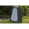 Tenda grigia alta e rettangolare con tetto arrotondato e porta con cerniera; cartello blu sulla porta con pittogrammi maschile e femminile; tiranti gialli; su erba vicino a un ruscello, circondata da alberi
