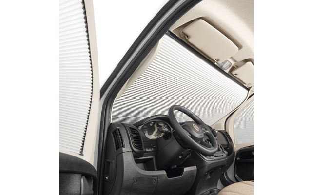 Vista interna lato guida di un veicolo con volante, cruscotto, quadro strumenti e un parasole argentato ripiegato che copre il parabrezza e il finestrino laterale