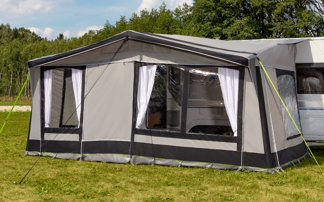 Weißer Wohnwagen mit angebrachter grauer Zelterweiterung auf grünem Rasen