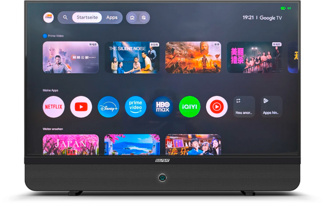 Televisore nero che mostra la schermata principale Google TV con ora 19:21, barra di ricerca, miniature di anteprima e icone delle app (Netflix, YouTube, Disney+, Prime Video, HBO Max, iQIYI). Piccola LED blu sulla cornice inferiore