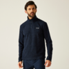 Mann mit blauem Pullover und dunkler Hose vor hellem Hintergrund