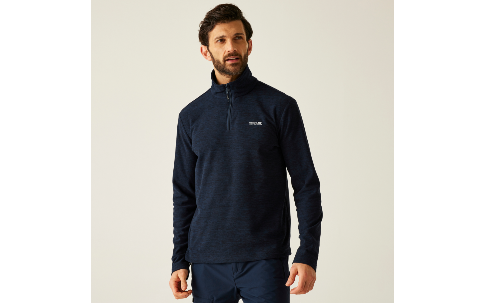 Mann mit blauem Pullover und dunkler Hose vor hellem Hintergrund