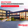 Plusieurs bâtiments au crépuscule avec fenêtres éclairées, un bassin et un parvis pavé ; grand texte rouge 'DEUTSCHES FAMILIENUNTERNEHMEN', bannière rouge 'SEIT 1956. KÜCHENHELFER FÜR DIE EWIGKEIT', logo 'WESTMARK' et slogan 'MACH'S EINFACH!'