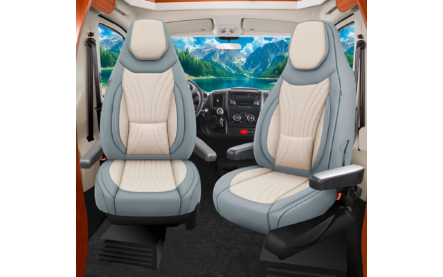 Zwei hellbeige Autositze mit graublauen Seiten und Armlehnen, schwarzer Boden, Lenkrad und Armaturenbrett; durch die Frontscheibe ein See vor Bergen und blauer Himmel mit Wolken