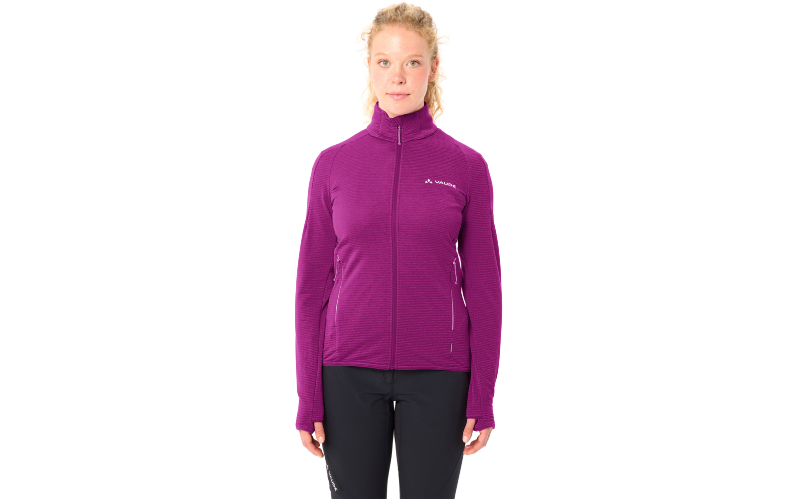 Person steht frontal, trägt violette Reißverschlussjacke mit hohem Kragen und Daumenlöchern, kleines Logo auf linker Brust, schwarze Hose, blonde Haare zu einem lockeren Dutt gebunden
