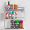 Gewürzregal mit verschiedenen Gewürzgläsern und einer Flasche Tabasco-Sauce, an einer weißen Wand montiert