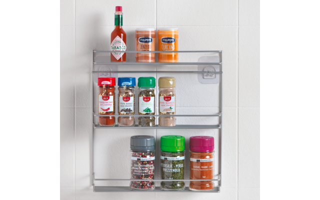 Gewürzregal mit verschiedenen Gewürzgläsern und einer Flasche Tabasco-Sauce, an einer weißen Wand montiert