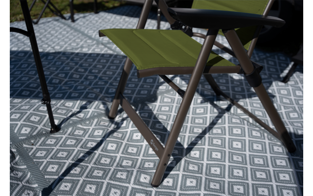 Groene opvouwbare kruk met bruin frame op grijs-wit vloerkleed met ruitpatroon, schaduwen en gedeeltelijke weergave van andere stoelpoten