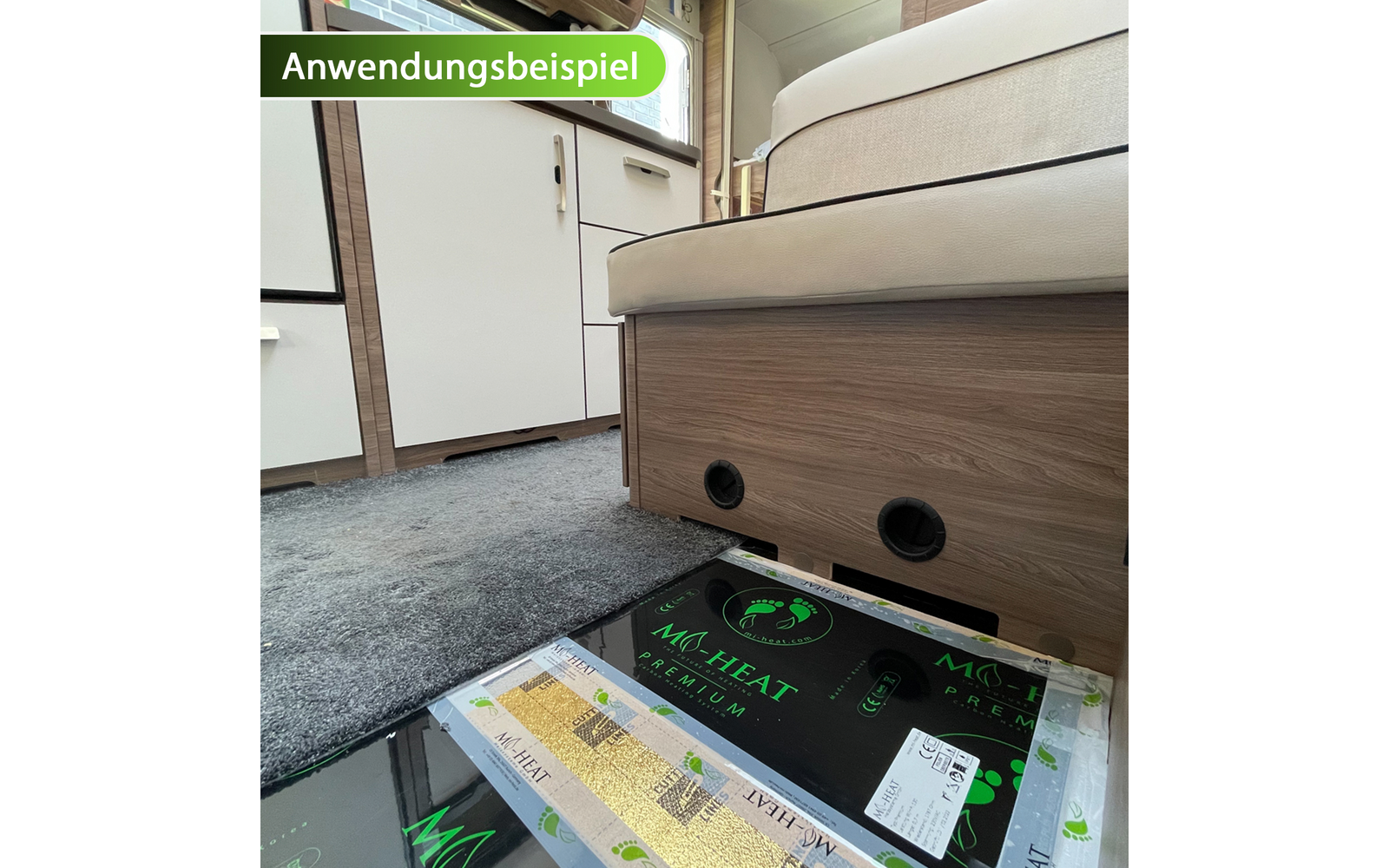 Bodennahe Ansicht eines Innenraums mit grauem Teppich, hell gepolstertem Sitz auf Holzkorpus mit zwei runden Öffnungen, weißen Schränken mit Griffen, reflektierender Verpackung mit schwarzem und grünem "Mi-Heat Premium"-Aufdruck und kleinem weißem Et