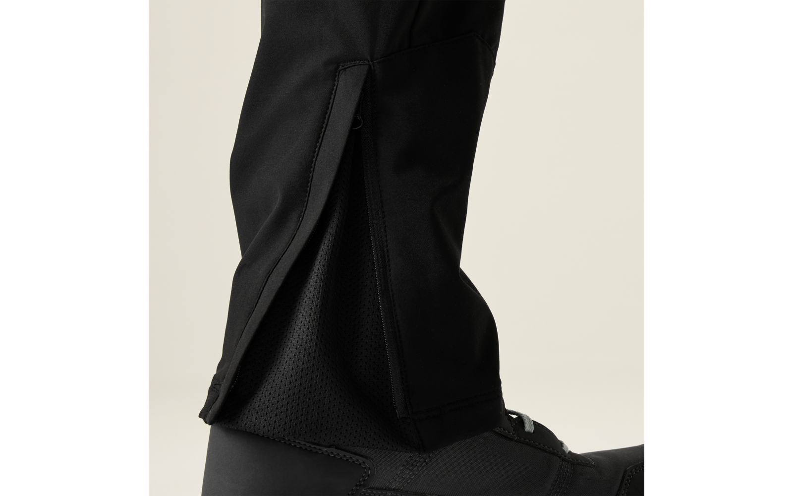 Close-up van een onderbeen in een zwarte broek met een open zijrits, zichtbaar donkere mesh-voering en een zwarte laars