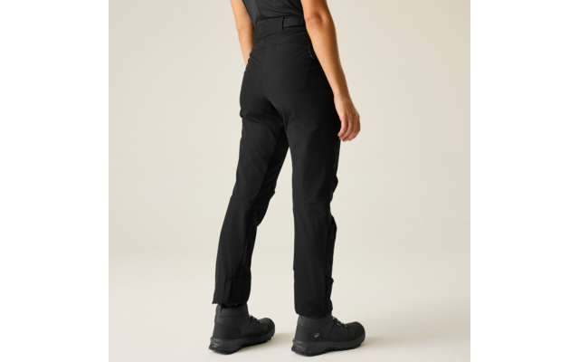 Achteraanzicht van een persoon van de taille naar beneden, zwarte outdoorbroek, zwarte enkellaarzen, lichte effen achtergrond