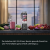 Mini-mixeur sans fil AEG sur plan de travail; à côté un verre de smoothie rose, récipient de mixage avec morceaux de fruits, bols avec raisins, fruits de la passion coupés en deux, quartiers de citron vert et tranches de fruit roses