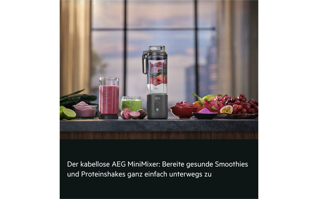 Mini-mixeur sans fil AEG sur plan de travail; à côté un verre de smoothie rose, récipient de mixage avec morceaux de fruits, bols avec raisins, fruits de la passion coupés en deux, quartiers de citron vert et tranches de fruit roses