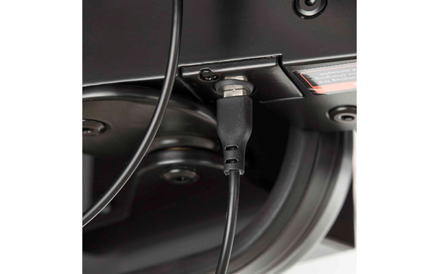 Nahaufnahme eines schwarzen Kabels, das in eine schwarze Buchse an der Unterseite eines Geräts gesteckt ist; sichtbare Schrauben und Metallbügel