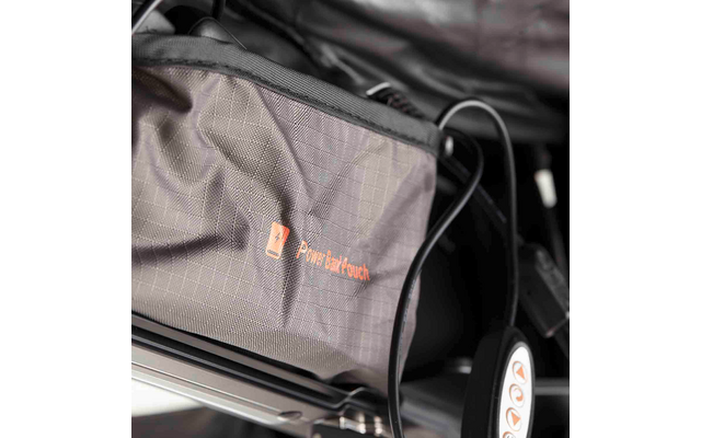 Grau strukturierte Stofftasche mit orangefarbenem Logo und Text 'Power Back Couch', an einem Metallrahmen befestigt; ein schwarzes Kabel verläuft daneben; ein Rad mit weißer Nabe und orangefarbener Markierung sichtbar