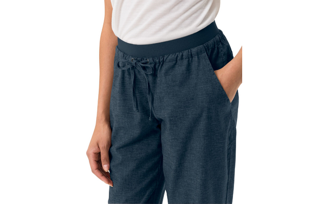 White top, dark blue fabric pants with elastic waistband, drawstring and side pockets; one hand in a pocket, one hand at the side