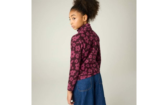 Person mit hochgestecktem lockigem Haar, trägt violett-rosa floral gemustertes Langarmoberteil und blauen Jeansrock, schaut über die Schulter, heller einfarbiger Hintergrund