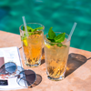Zwei Gläser mit Eistee und Minzblättern auf einem Tisch neben einer Sonnenbrille am Pool