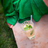 Ein Glas mit Getränk und Minzblättern auf einer Marmorplatte, im Hintergrund eine grüne Decke und eine nackte, sitzende Person