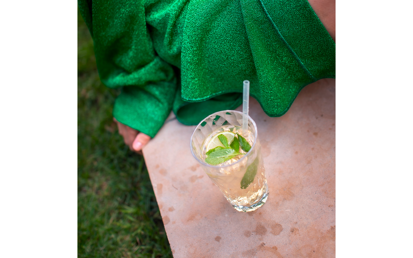 Ein Glas mit Getränk und Minzblättern auf einer Marmorplatte, im Hintergrund eine grüne Decke und eine nackte, sitzende Person