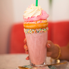 Ein rosa Milchshake mit Sahne und einem Keks, gehalten von einer Hand