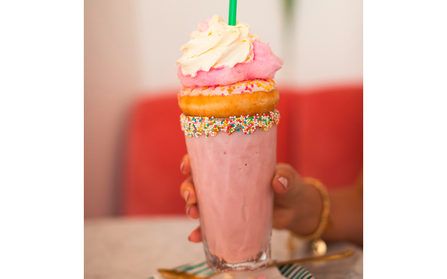 Ein rosa Milchshake mit Sahne und einem Keks, gehalten von einer Hand