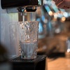 Ein Glas unter einer Kaffeemaschine, das mit Wasser gefüllt wird