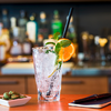 Ein Glas mit einem Cocktail, garniert mit einer Orangenscheibe und Minze, auf einem Tisch vor einer Bar
