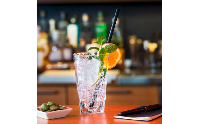 Ein Glas mit einem Cocktail, garniert mit einer Orangenscheibe und Minze, auf einem Tisch vor einer Bar