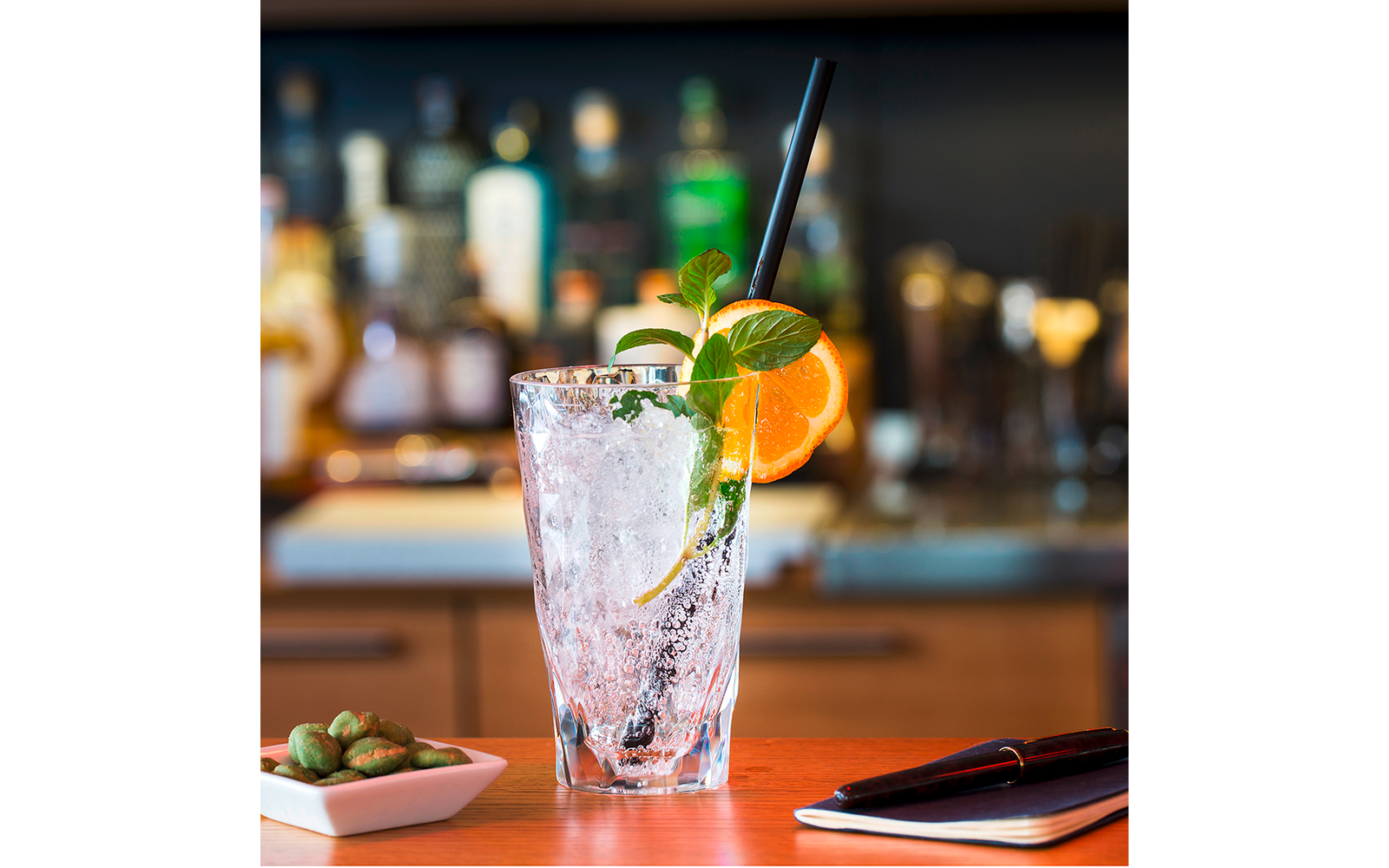 Ein Glas mit einem Cocktail, garniert mit einer Orangenscheibe und Minze, auf einem Tisch vor einer Bar