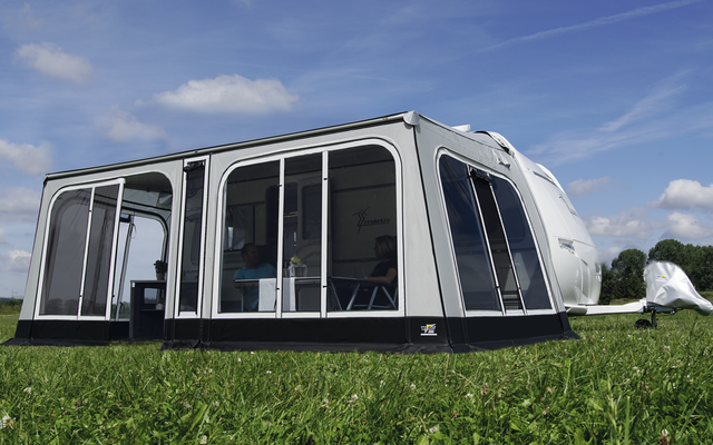 Caravane avec auvent transparent attaché sur une prairie verte sous un ciel bleu
