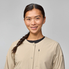 Person mit seitlichem Zopf, beige knopfbare Jacke und schwarzes Oberteil, leichtes Lächeln, hellgrauer Hintergrund