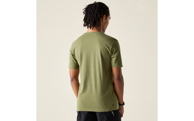 Person von hinten mit Dreadlocks, trägt olivgrünes T‑Shirt mit kurzen Ärmeln und schwarze Shorts, heller beiger Hintergrund