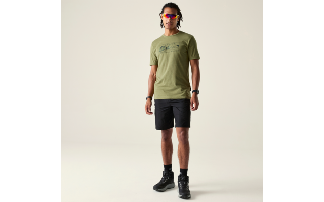 Person steht frontal, trägt olivgrünes T-Shirt mit Print, schwarze Shorts, schwarze Stiefel, bunte Sonnenbrille und geflochtene Haare vor hellem Hintergrund