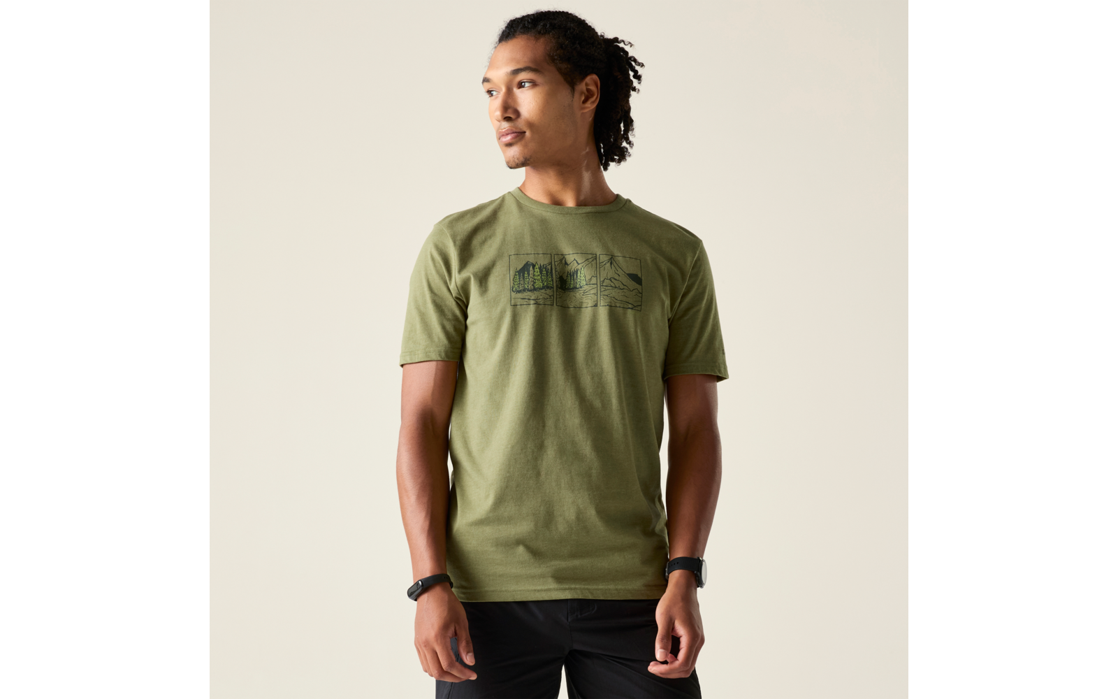 Mann mit zurückgebundenen Haaren in olivgrünem T‑Shirt und schwarzer Hose vor hellem Hintergrund, blickt nach links