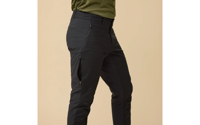 Bovenlichaam en benen van een persoon, olijfgroen T‑shirt, zwarte broek met ritssluiting op de dij, beige achtergrond