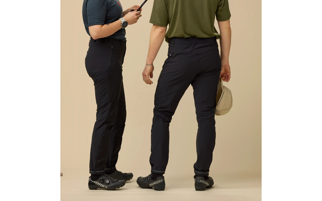 Twee personen zichtbaar van taille naar beneden, dragen donkere broeken en fietsschoenen; links houdt iemand een apparaat vast, rechts iemand een beige pet