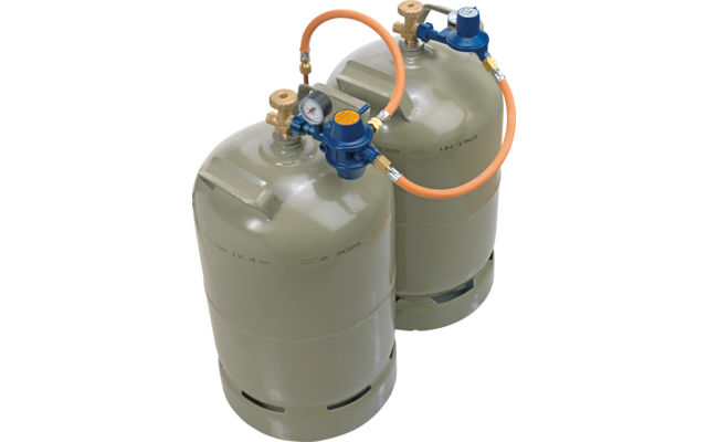 Dos bombonas de gas gris verdoso de pie, con reguladores de presión azules, un manómetro y una manguera de conexión naranja