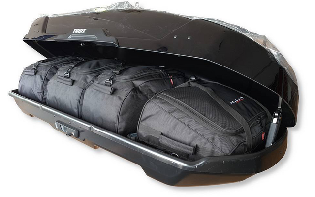 Coffre de toit noir ouvert contenant plusieurs sacs de voyage et sacs à dos noirs sur fond blanc