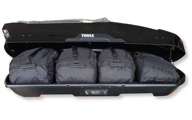 Coffre de toit noir ouvert avec le logo «Thule» visible et quatre sacs de voyage noirs à l'intérieur