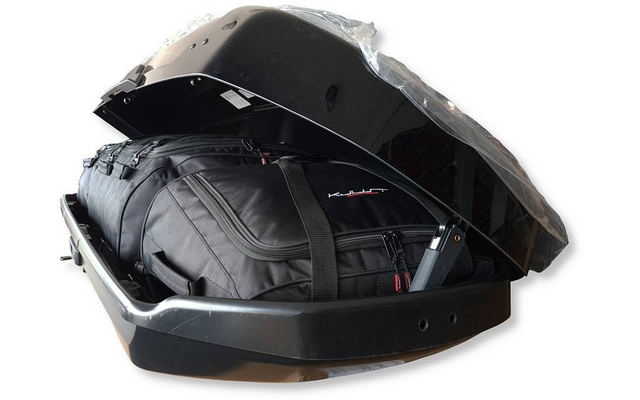 Coffre de toit noir ouvert avec un sac de voyage noir et des sangles à l'intérieur