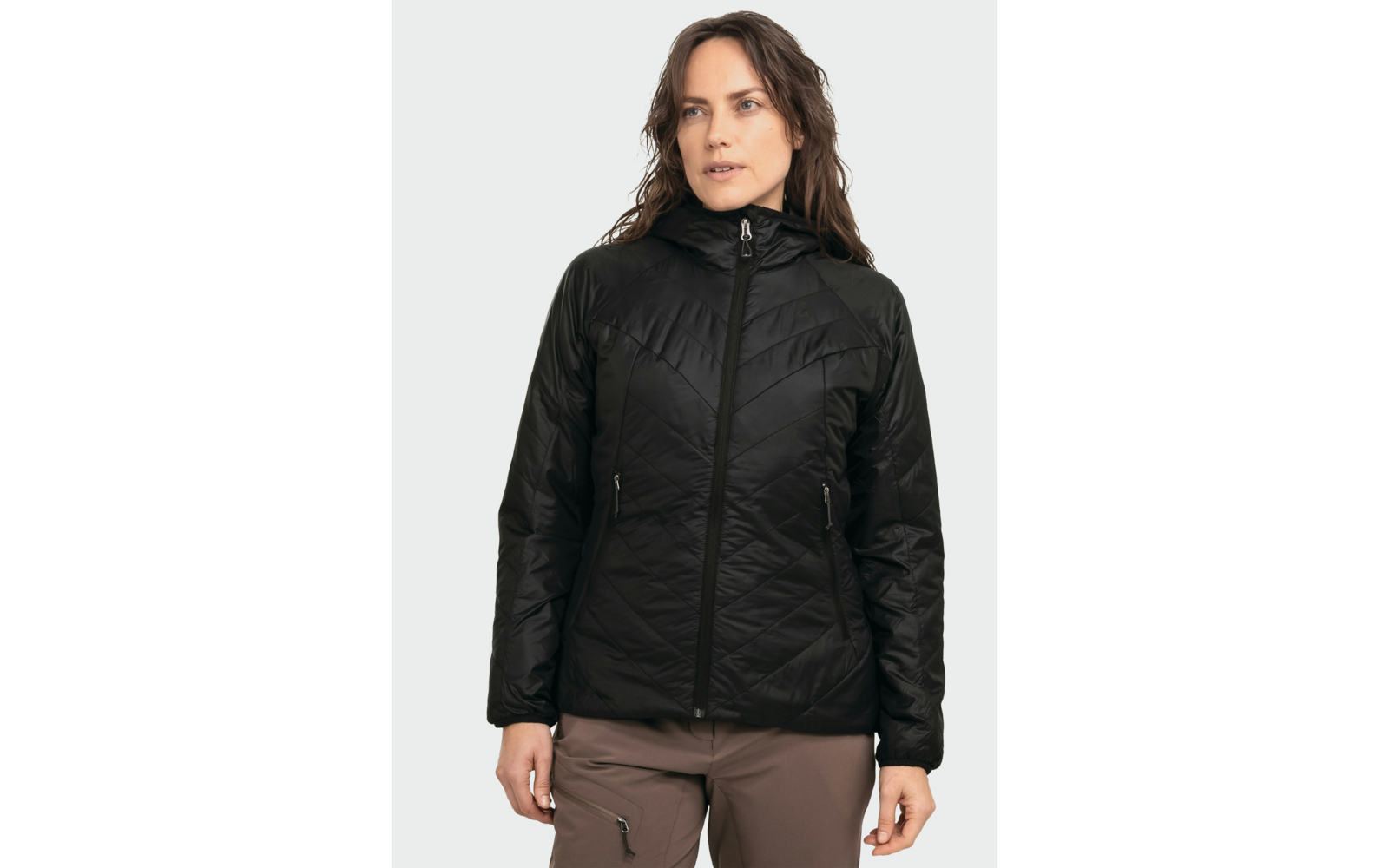 Person in schwarzer gesteppter Jacke mit Kapuze und Reißverschluss, braune Hose, heller Hintergrund