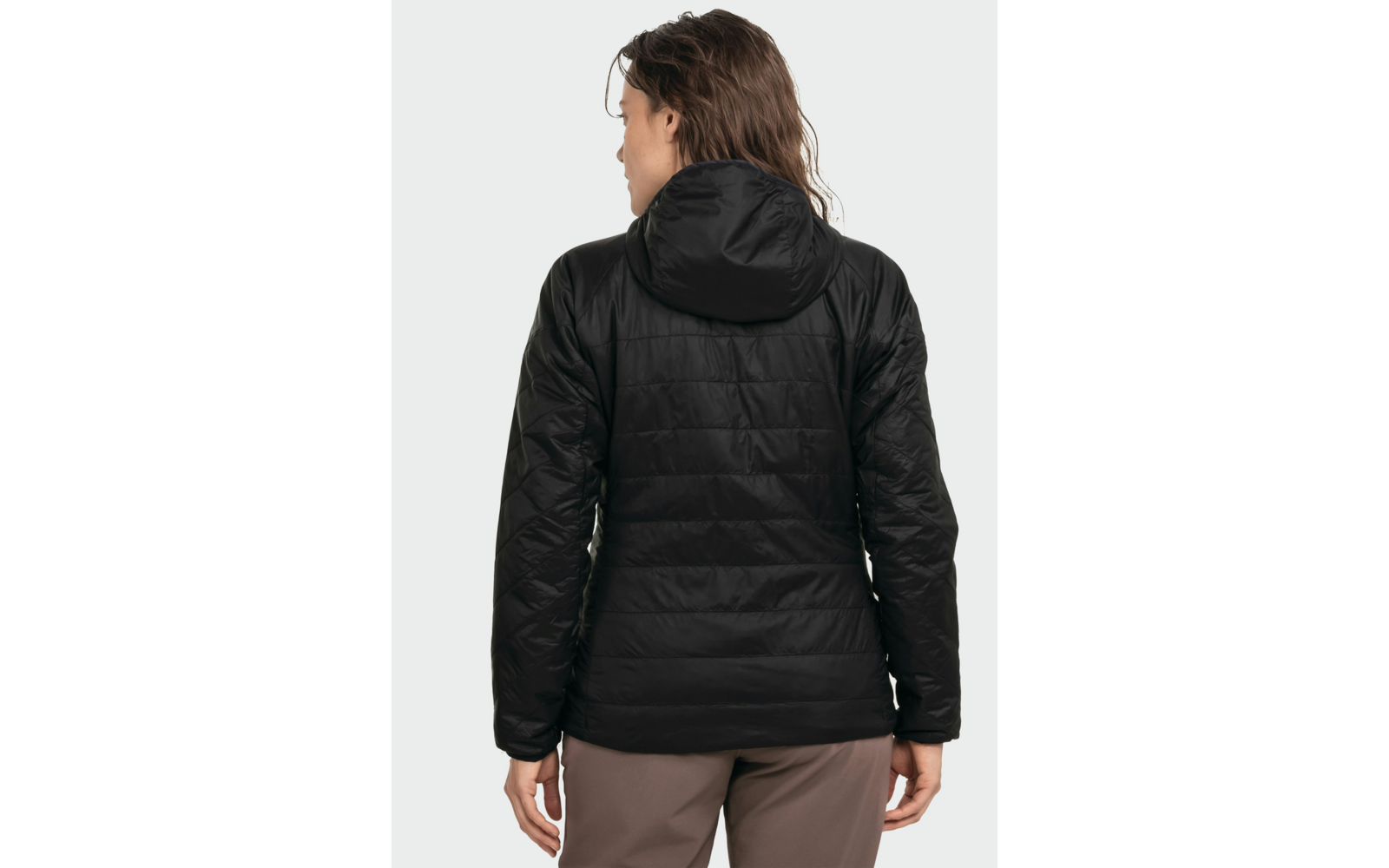 Person von hinten, schwarze gesteppte Jacke mit Kapuze, braune Hose, schulterlange braune Haare, heller grauer Hintergrund