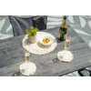 Table grise avec une bouteille à capsule dorée, deux verres remplis, un bol blanc avec trois brochettes, une petite plante en pot et des sets de table crochetés ; chaise grise en arrière-plan