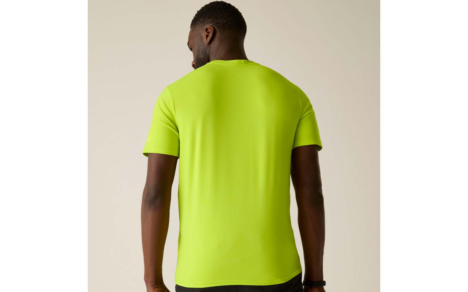 Persoon van achteren gezien draagt neongroen T-shirt, zichtbare armen, beige achtergrond