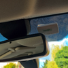 Innenraum eines Autos mit Rückspiegel; oberhalb des Spiegels an der Windschutzscheibe ein kleines weißes Kästchen; punktierte Folie am Glas; draußen Bäume und blauer Himmel