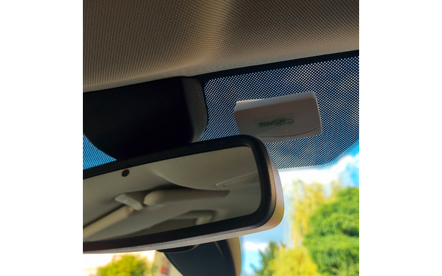 Innenraum eines Autos mit Rückspiegel; oberhalb des Spiegels an der Windschutzscheibe ein kleines weißes Kästchen; punktierte Folie am Glas; draußen Bäume und blauer Himmel