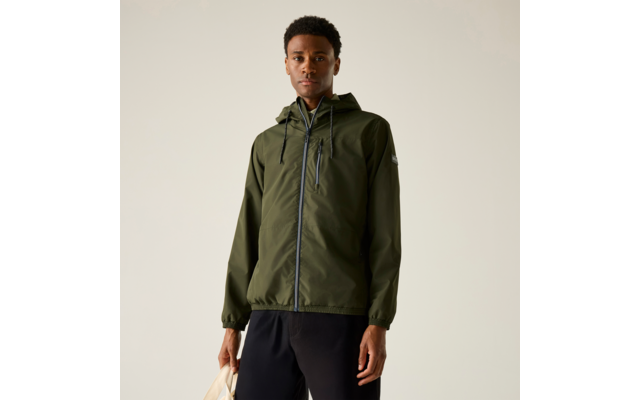 Person steht vor hellem Hintergrund, trägt olivgrüne Kapuzenjacke mit Reißverschluss und schwarze Hosen, hält eine helle Tasche in der linken Hand