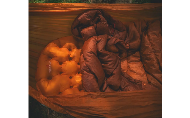 Close-up van een bed met een gekreukelde bruine deken en een oranje kussen op een houten oppervlak