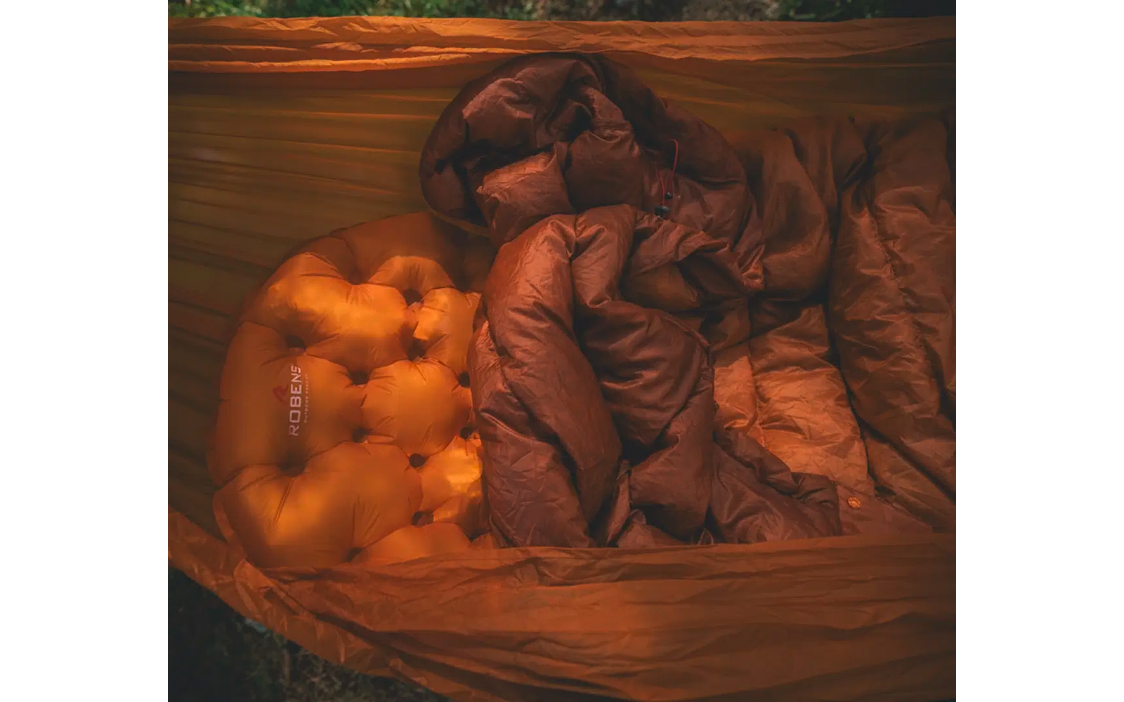 Close-up van een bed met een gekreukelde bruine deken en een oranje kussen op een houten oppervlak